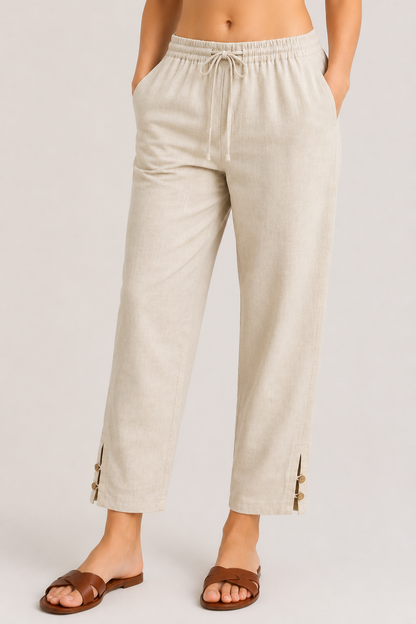A person wearing light beige drawstring pants with side buttons and brown slide sandals, shown from the waist down against a plain light gray studio background.